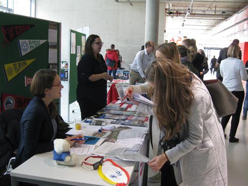 Students speaking to 2 representatives of outgoing insitutions at a desk with Information material
